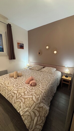 A hotel room with a large bed, a nightstand with a lamp, and a window with curtains. - Gîte l'olivade For 4 pers private pool (Flayosc)