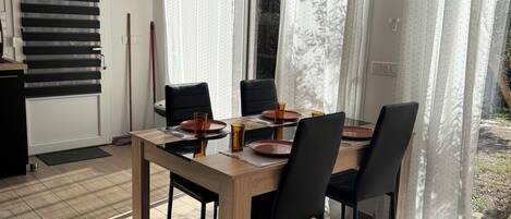 Un coin repas avec une table et des chaises en bois, une fenêtre avec des rideaux et une vue sur l’extérieur.