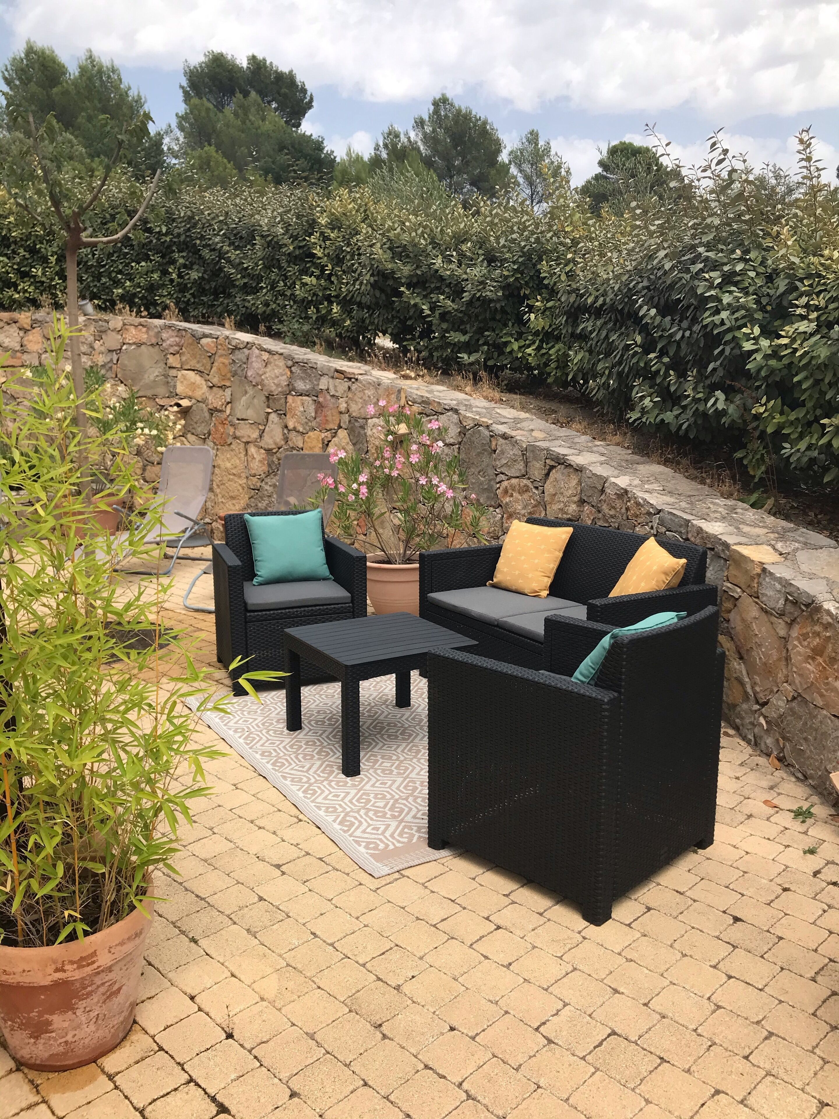 An outdoor seating area with a stone wall, a potted plant, and a view of the surrounding greenery.