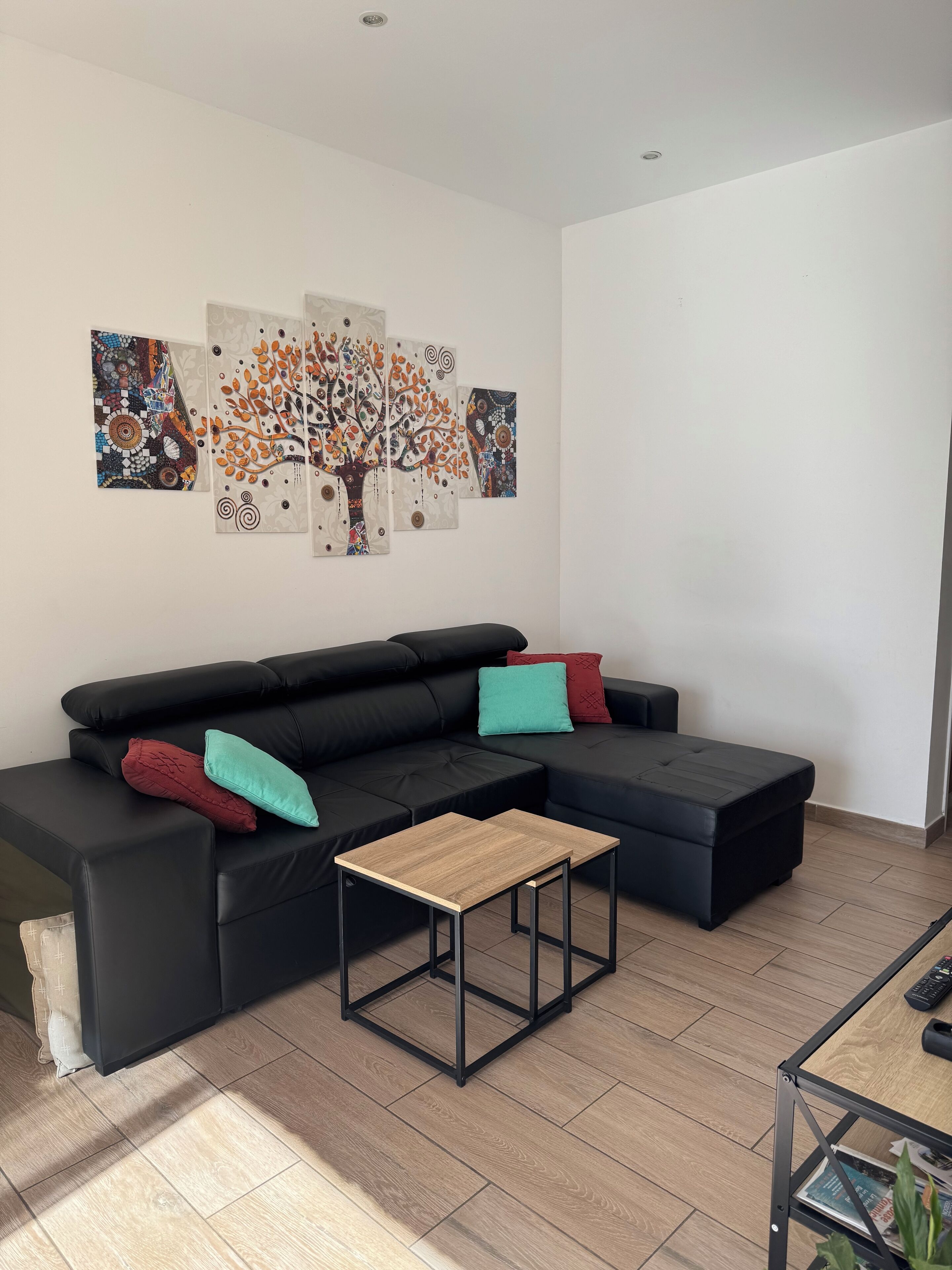 A modern living room with a black sectional sofa, a small wooden coffee table, and a wall-mounted abstract art piece.