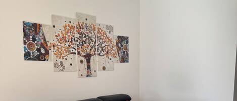 A modern living room with a black sectional sofa, a small wooden coffee table, and a wall-mounted abstract art piece.
