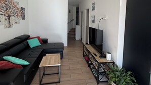 A modern living room with a black sofa, a wooden coffee table, and a TV on a stand. There is a staircase leading to another level.