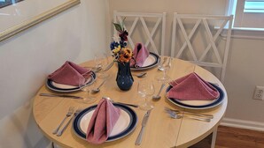 Une table à manger dressée pour quatre personnes, avec un vase de fleurs, des assiettes, des couverts et des serviettes.