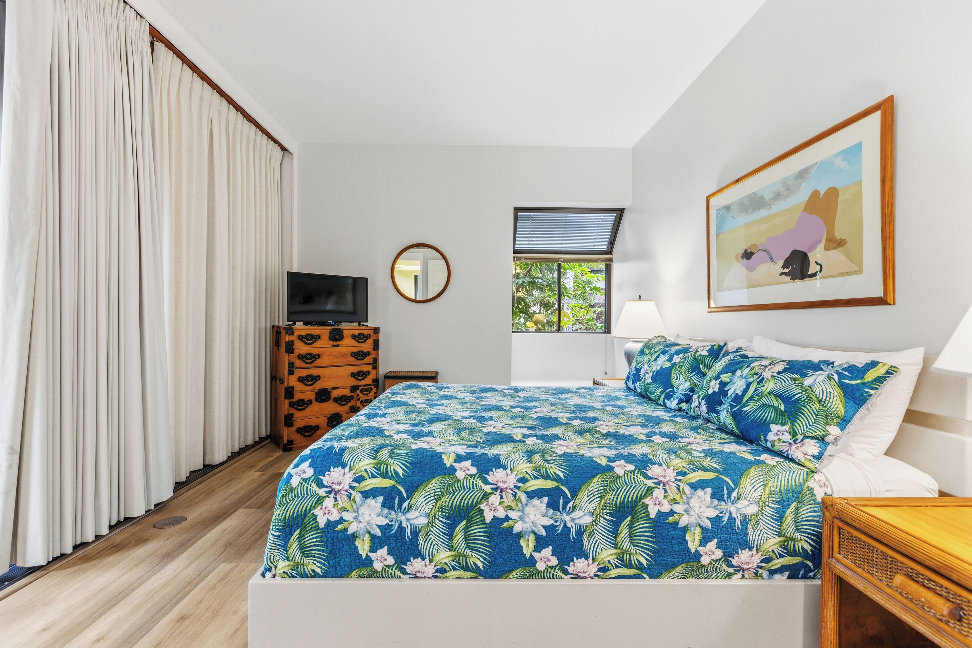 A bedroom with a bed, a dresser, a television, a window, and a painting on the wall.