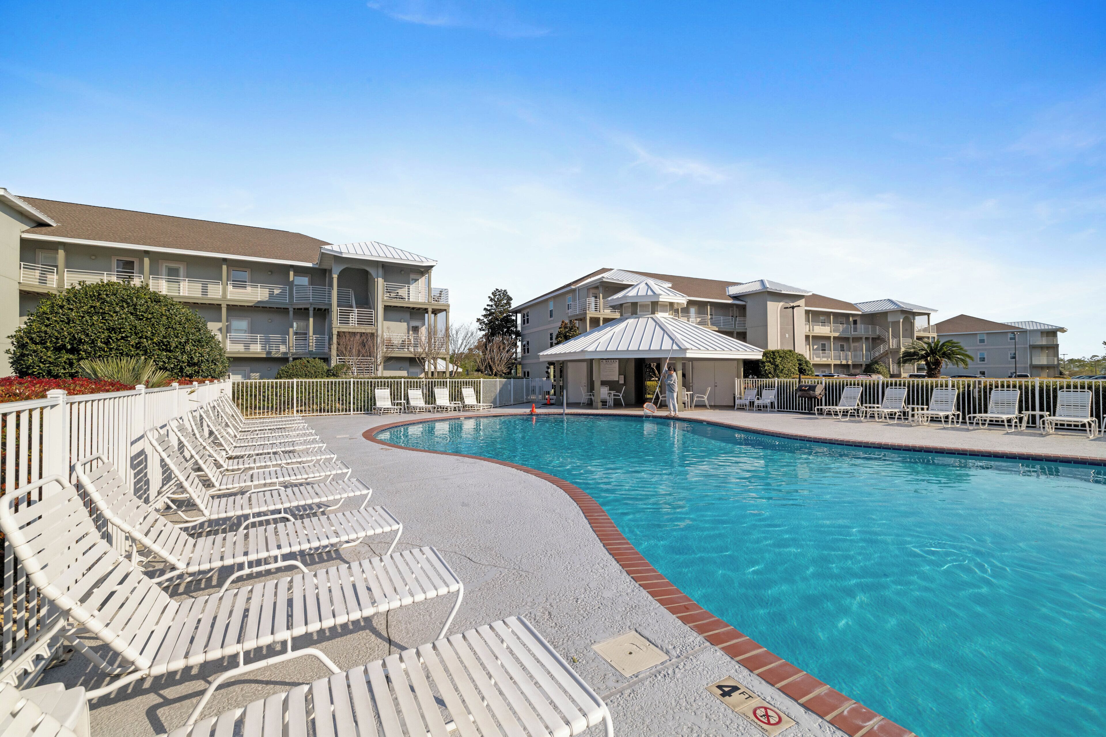 A swimming pool with lounge chairs, a covered area, and a building with multiple balconies.