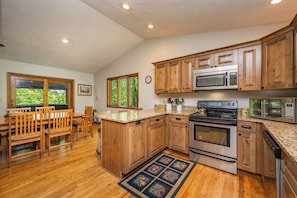 A kitchen with wooden cabinets, a stainless steel stove, a microwave, and a dining area with wooden furniture.