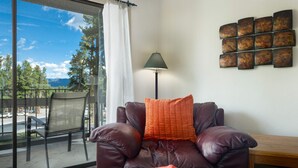 Ein Ledersofa mit Buch, Lampe und Wandbild in einem Raum mit großem Fenster und Blick auf Bäume und Berge.