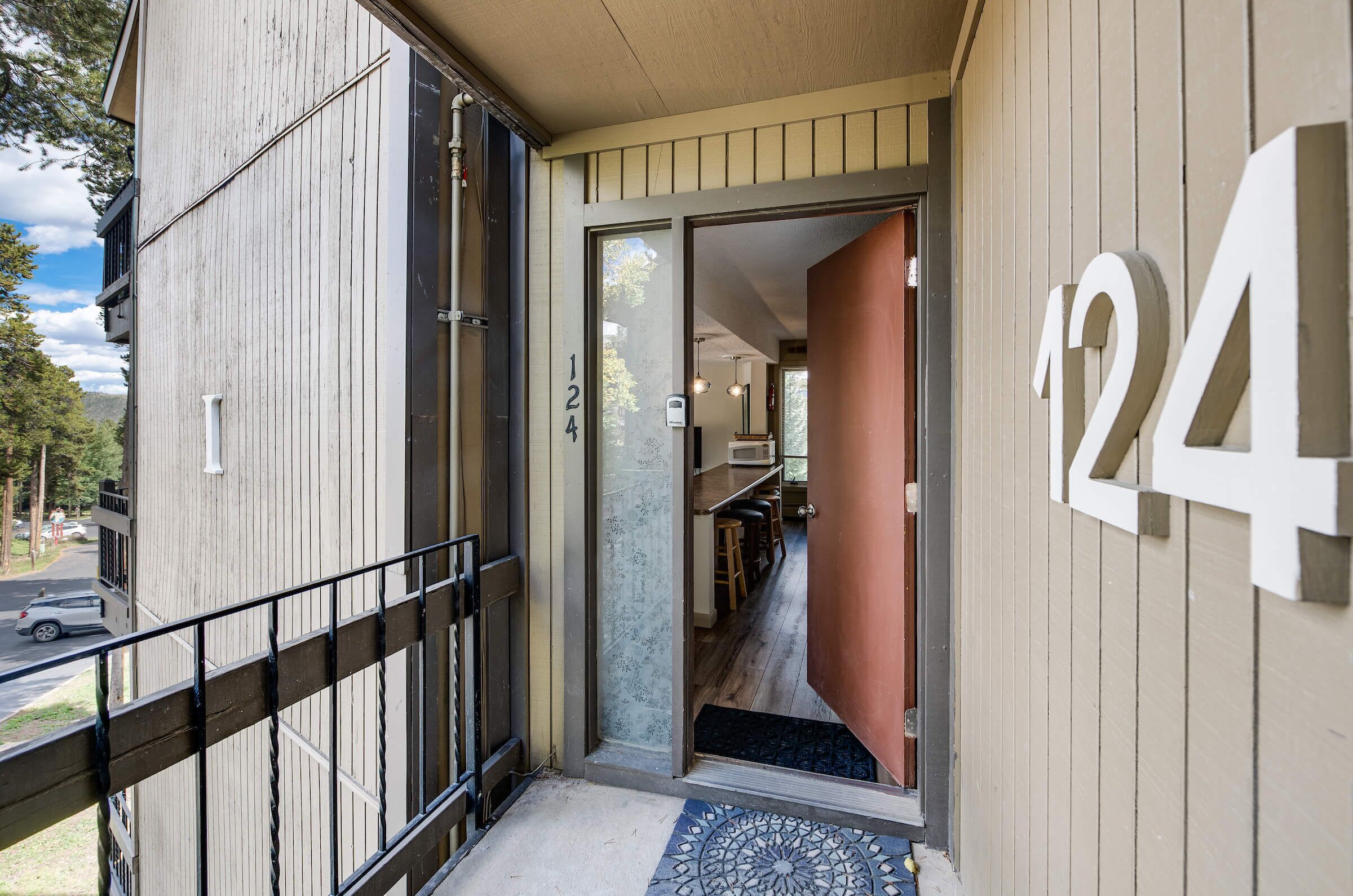 Une entrée d’immeuble avec une plaque portant le numéro 24, une porte en verre et un petit espace extérieur agrémenté d’une rambarde en métal.