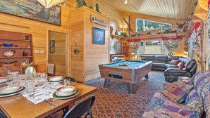 Un interior de cabaña acogedor con una mesa de billar, un sofá de cuero y una zona de comedor con mesa y sillas de madera.