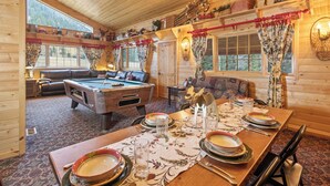 Un acogedor interior de cabaña de madera con mesa de billar, mesa de comedor para cuatro personas y chimenea.