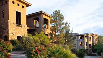 A multi-story building with balconies and a stone facade, surrounded by landscaped gardens and trees.