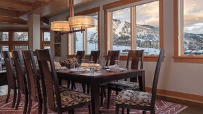 Un coin repas avec une table dressée pour six personnes, de grandes fenêtres offrant une vue sur les montagnes et des poutres en bois au plafond.