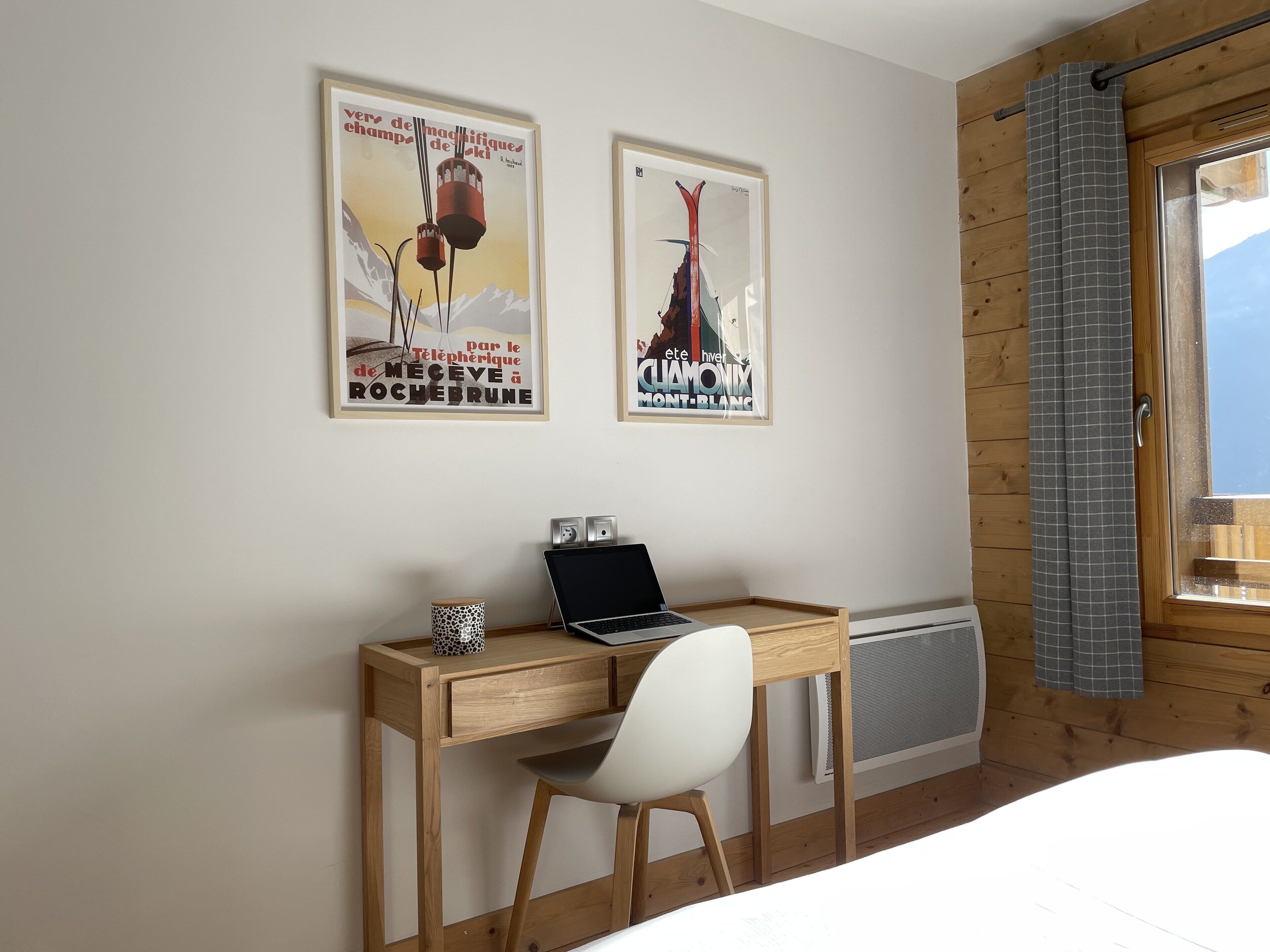 Un bureau en bois avec un ordinateur portable et une chaise, dans une pièce aux murs en bois et dotée d’une fenêtre avec des rideaux.