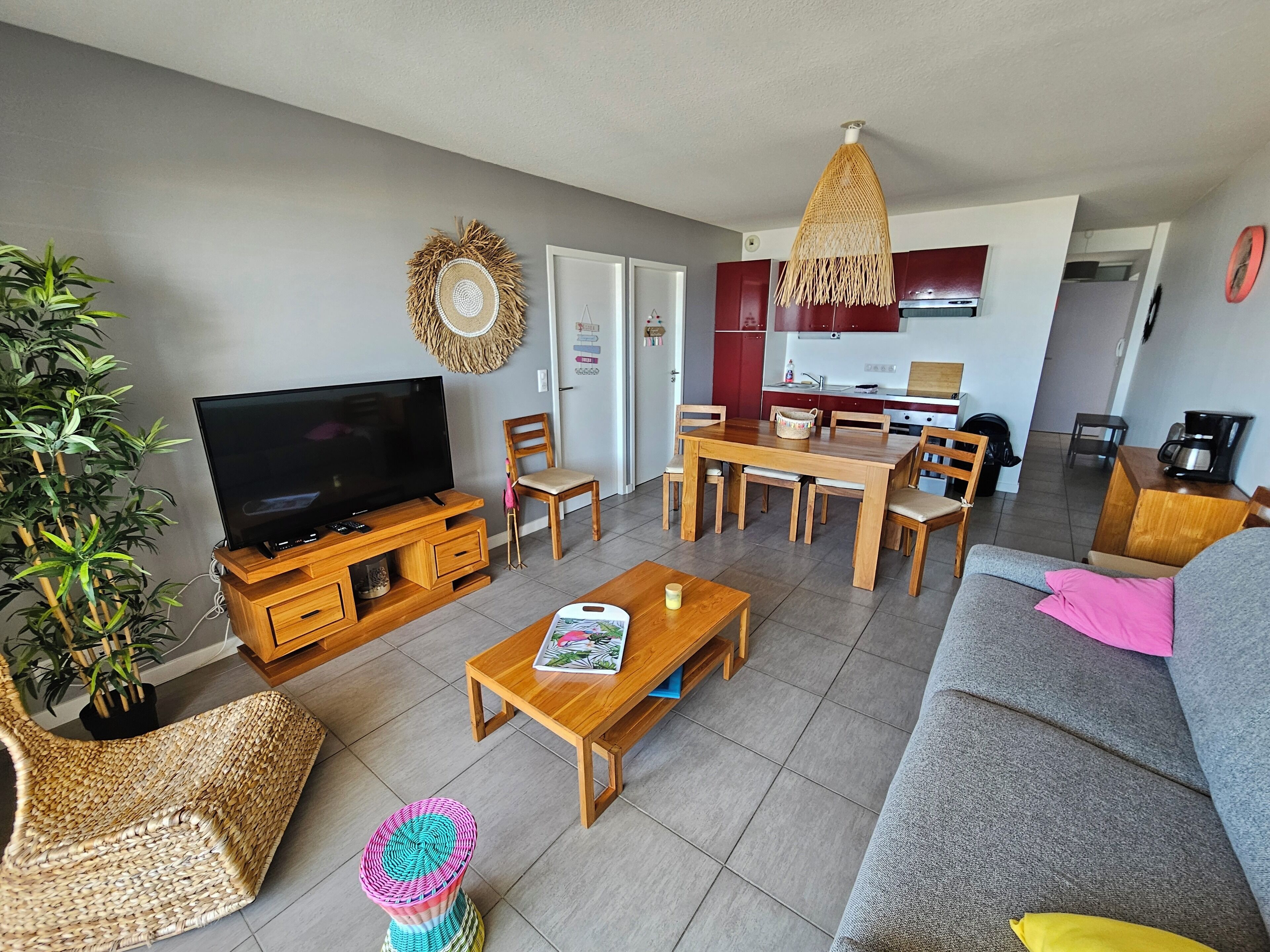 A living room with a TV, wooden furniture, a dining table, and a kitchen in the background.