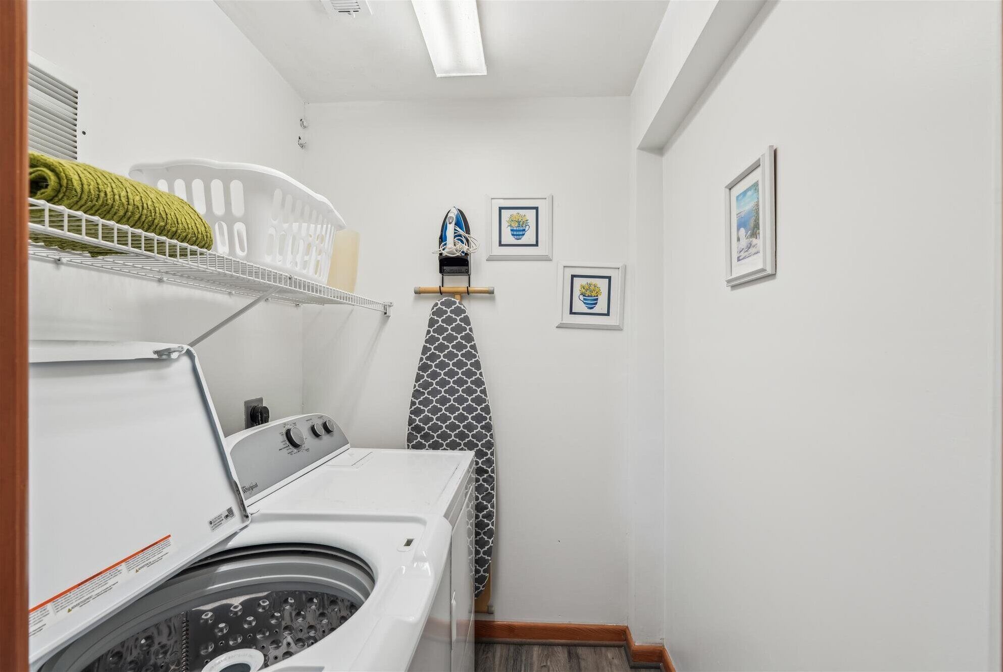 Une buanderie équipée d’un lave-linge à chargement frontal, d’un étendoir et d’une petite planche à repasser.