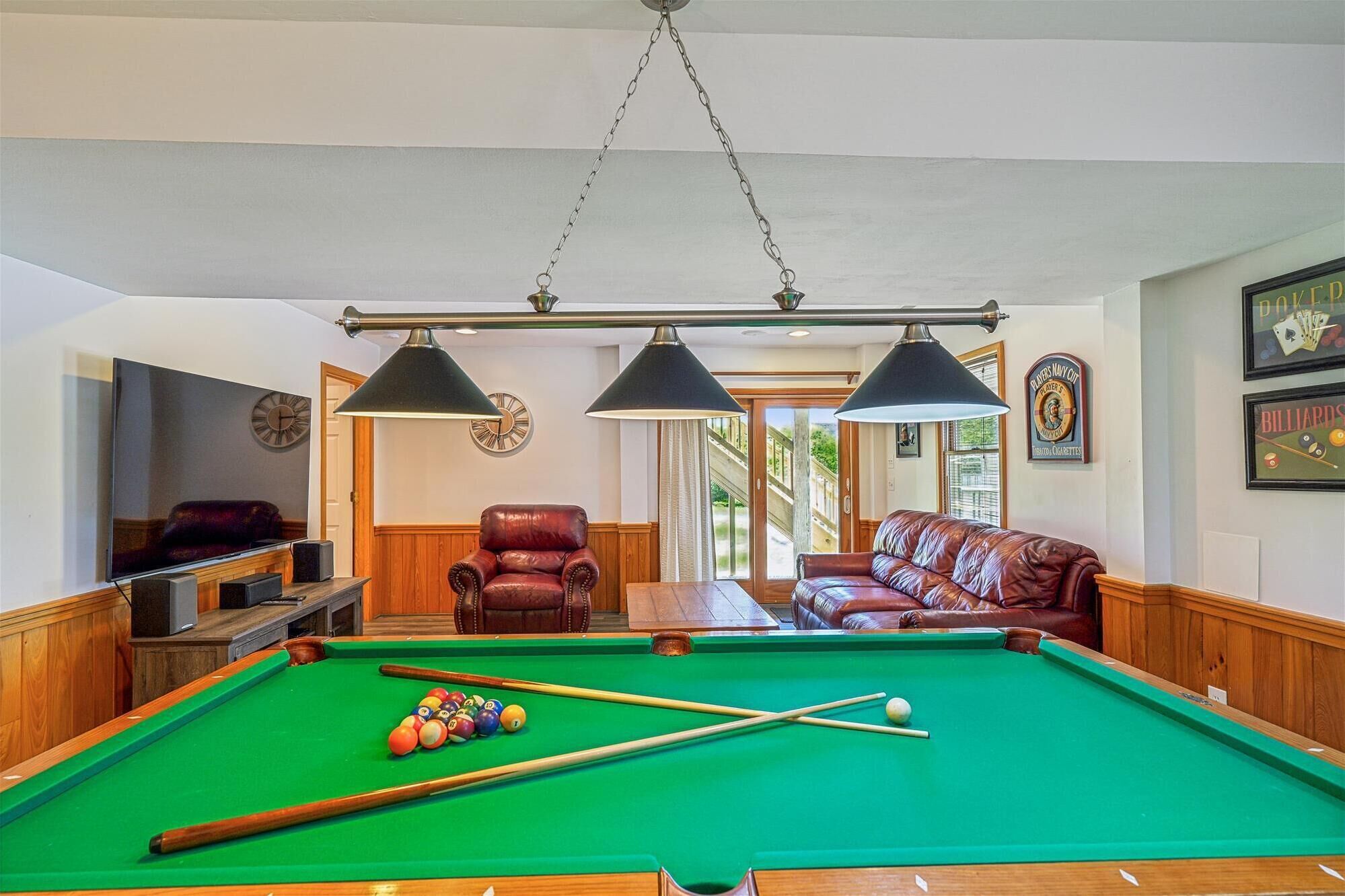 Ein Billardtisch mit Kugeln, ein Fernseher und zwei Ledersessel in einem Raum mit Holzwänden und einer Wand mit Billard-Motiven.