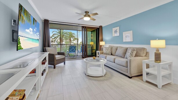 A living room with a sofa, armchairs, a coffee table, a TV, and a balcony with a view.