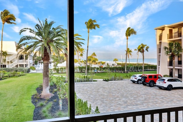 A hotel courtyard with palm trees, a paved area, and a view of the beach.