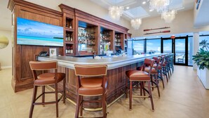 A bar area with wooden cabinetry, bar stools, and a large TV screen displaying a beach scene.