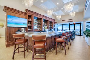 A bar area with wooden cabinetry, bar stools, and a large TV screen displaying a beach scene.