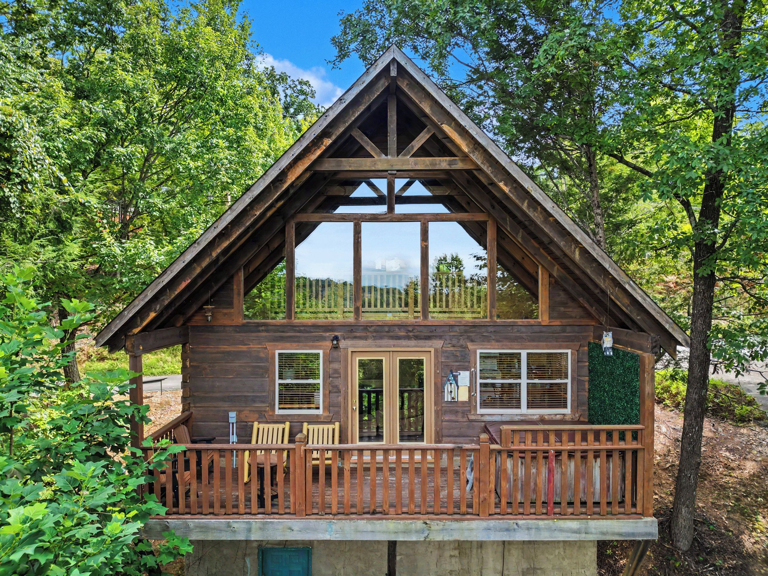A wooden cabin with a balcony, large windows, and a deck with chairs.