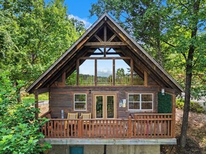 A wooden cabin with a balcony, large windows, and a deck with chairs.