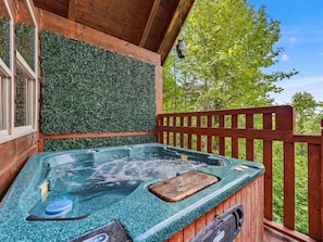 Un bain à remous doté d’une terrasse en bois et d’une rambarde en bois, le tout entouré de verdure.