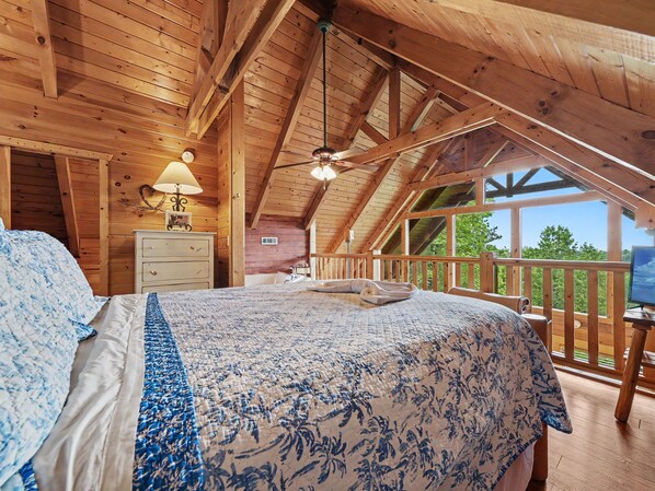 A bedroom with a bed, a nightstand, a lamp, a dresser, and a view of the outdoors.