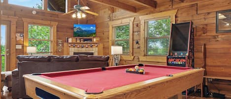 A wooden interior with a pool table, a television, and a fireplace.