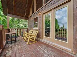 Eine Holzterrasse mit Schaukelstühlen und einem Tisch, mit Blick auf ein bewaldetes Gebiet.