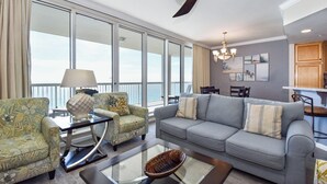 A spacious living room with a grey sofa, patterned armchairs, a glass coffee table, and a view through large windows. - A three-bedroom beachfront, modern Gulf Coast getaway! 🌴 (Destin)