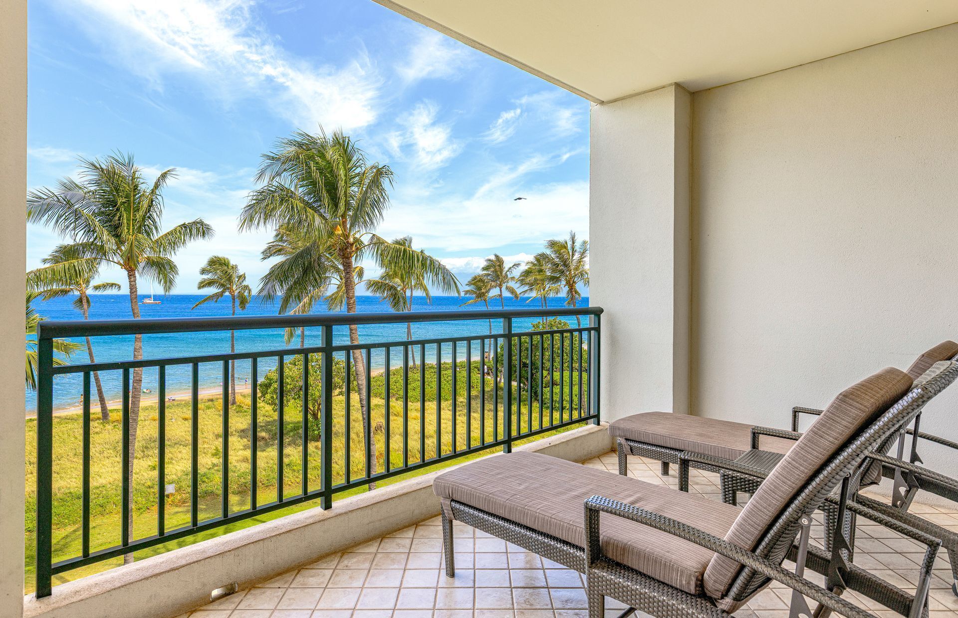 Een balkon met uitzicht op de oceaan en palmbomen, met twee rieten stoelen.