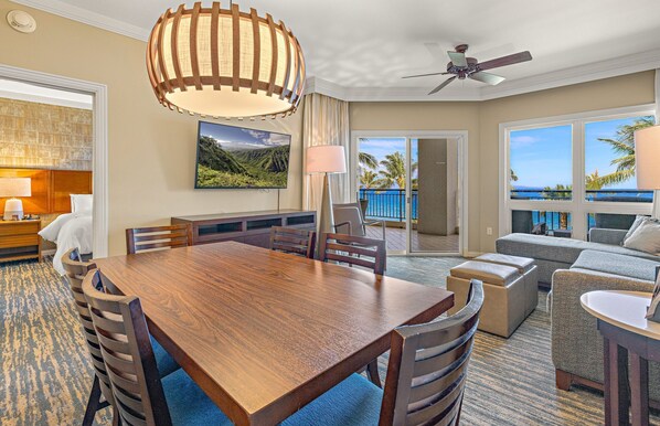 A hotel room with a dining area, a sofa, a ceiling fan, and a view of the ocean.