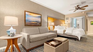 A hotel room with a sofa, a bedside table with a lamp, a bed with white bedding, a ceiling fan, and a painting on the wall. - Maui Resort Rentals: Westin Ka'anapali Ocean Resort 2BR Direct Oceanfront Villa (Lahaina)