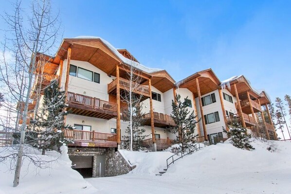 Eine mehrstöckige Lodge mit hölzernen Balkonen und einer Skipiste im Vordergrund.