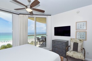 A bedroom with a bed, a ceiling fan, a dresser, a chair, a TV, and a balcony with a view of the beach. - Updated chic, modern beachfront condo w/private balcony! (Destin)