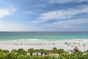 A beach with umbrellas and lounge chairs, a small hut, and palm trees. - Updated chic, modern beachfront condo w/private balcony! (Destin)
