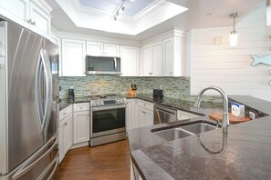 A modern kitchen with white cabinetry, stainless steel appliances, a tiled backsplash, and a skylight. - Updated chic, modern beachfront condo w/private balcony! (Destin)