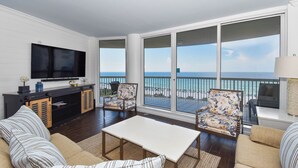 A living room with a TV, sofa, chairs, and a balcony with a view of the ocean. - Updated chic, modern beachfront condo w/private balcony! (Destin)