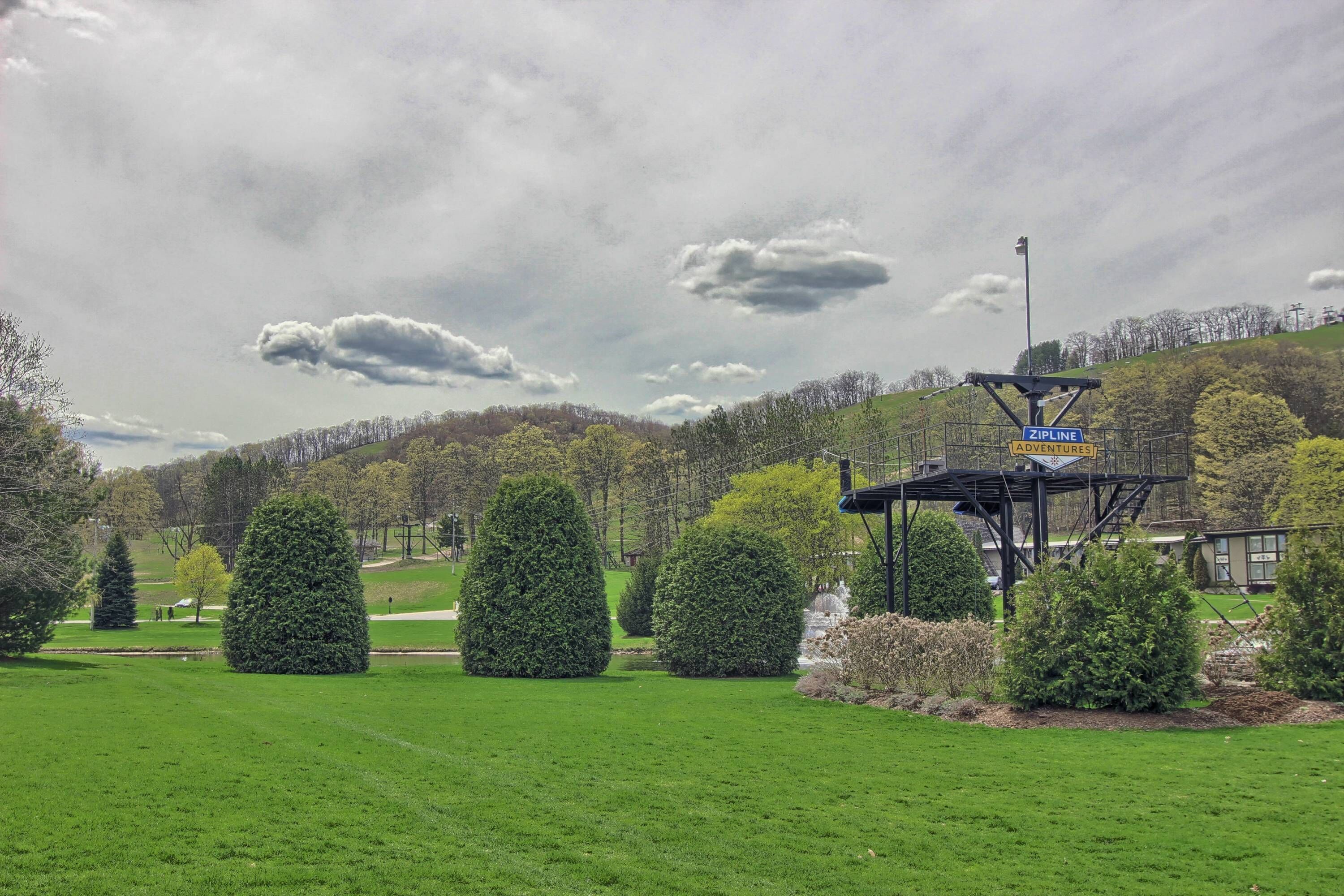 A park with a zipline attraction, well-maintained grass, and neatly trimmed trees.