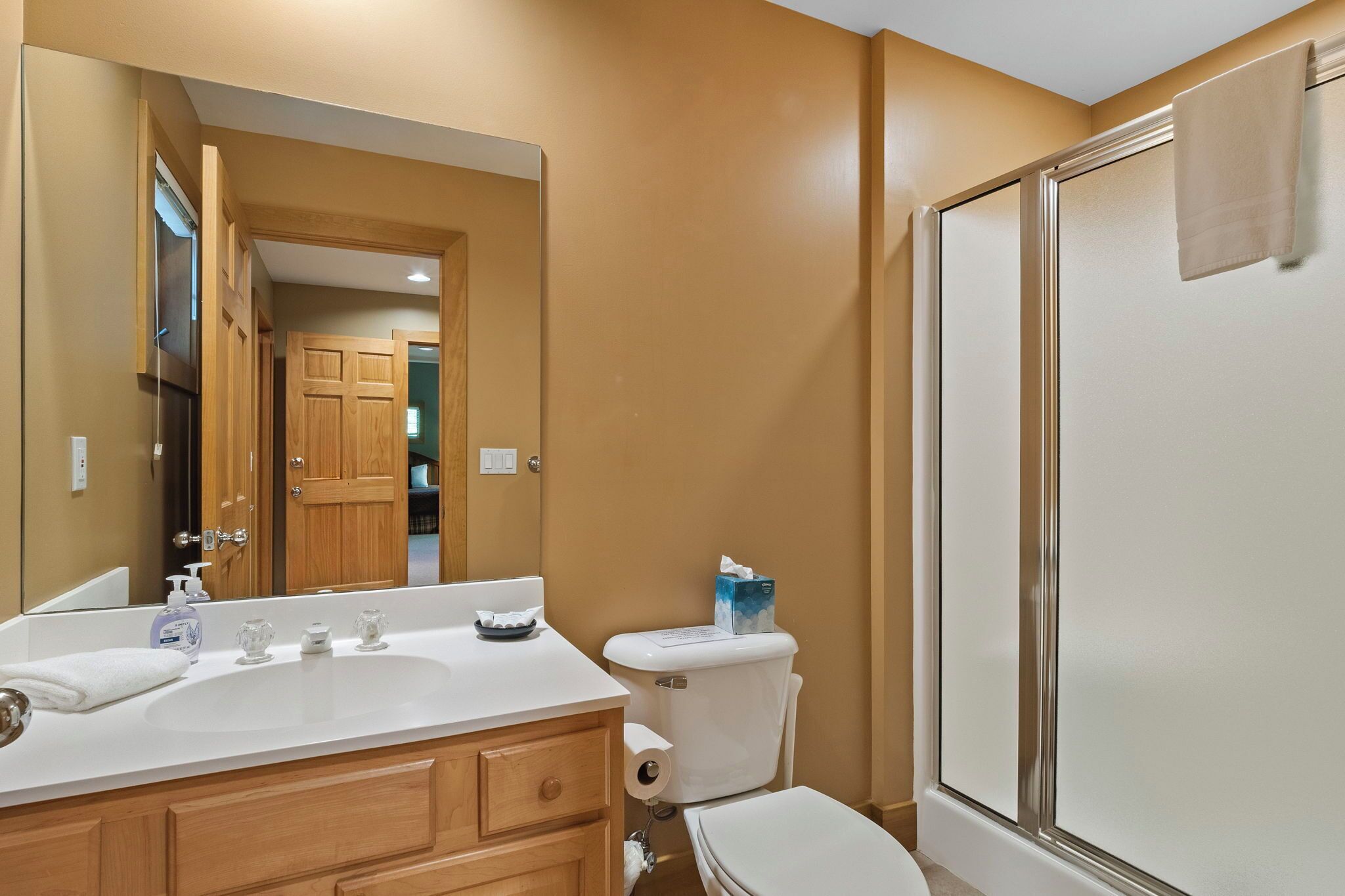 A bathroom with a white sink, wooden cabinets, a toilet, and a glass shower enclosure.