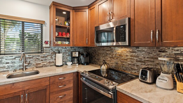 A modern kitchen with wooden cabinets, a stainless steel microwave, a stove, a toaster, and a blender. - Corner Beachfront Delight: Kihei Beach 110 Convenient Ground-Floor Haven! (Kihei)