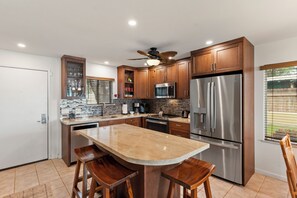 Una cocina moderna con armarios de madera, electrodomésticos de acero inoxidable, encimera de mármol y ventilador de techo.