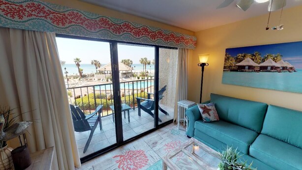 Ein Zimmer mit Balkon, einem türkisfarbenen Sofa, einem Couchtisch und einem Strandbild.