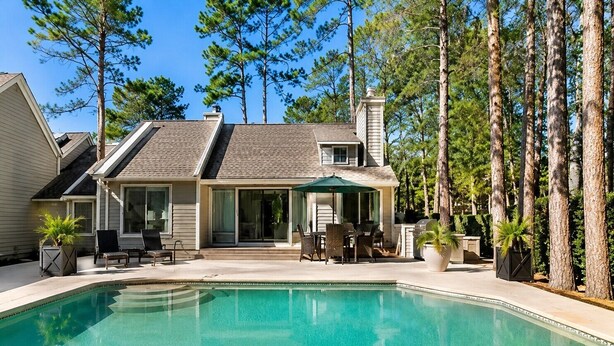 A house with a swimming pool, a patio with outdoor furniture, and tall trees in the background. - 21 Windjammer-Private Pool, views of the 10th tee of Harbour Town Golf Links (Hilton Head Island)