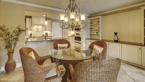 A dining area with a glass table surrounded by wicker chairs, a chandelier, and a kitchen in the background. - 21 Windjammer-Private Pool, views of the 10th tee of Harbour Town Golf Links (Hilton Head Island)