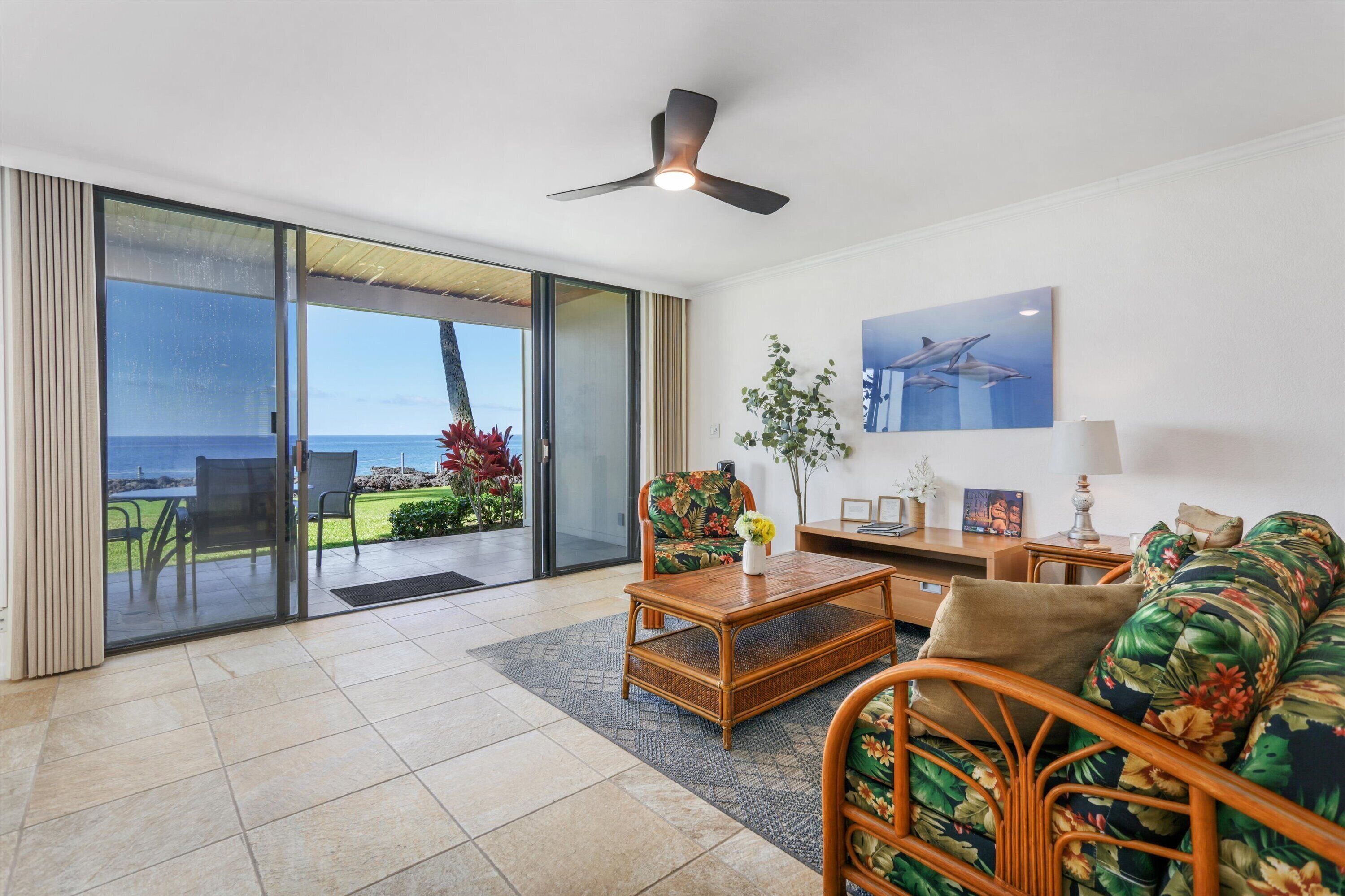 A modern living room with a large sliding glass door leading to a balcony, a ceiling fan, a sofa, a coffee table, and a small side table with a lamp.