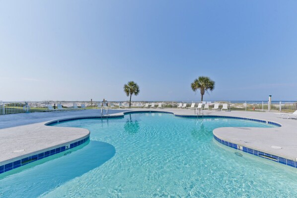 Une piscine d’un bleu éclatant, à bords incurvés, entourée d’une clôture blanche et de chaises longues.
