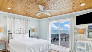 A bedroom with a wooden ceiling, a bed with white bedding, a desk with a chair, and a view of the ocean through a large window. - Gulf Front Retreat | Screened Porch | Fort Morgan Escape (Gulf Shores)