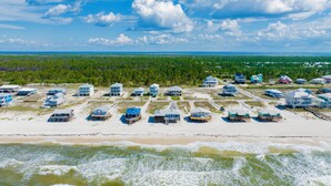 A coastal area with beach houses, some elevated on stilts, and a forested background. - Gulf Front Retreat | Screened Porch | Fort Morgan Escape (Gulf Shores)